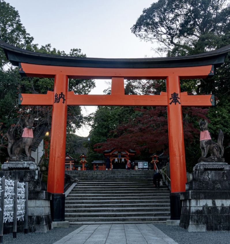 Vermilion torii gate at Fushimi Inari Shrine in Kyoto, flanked by fox statues